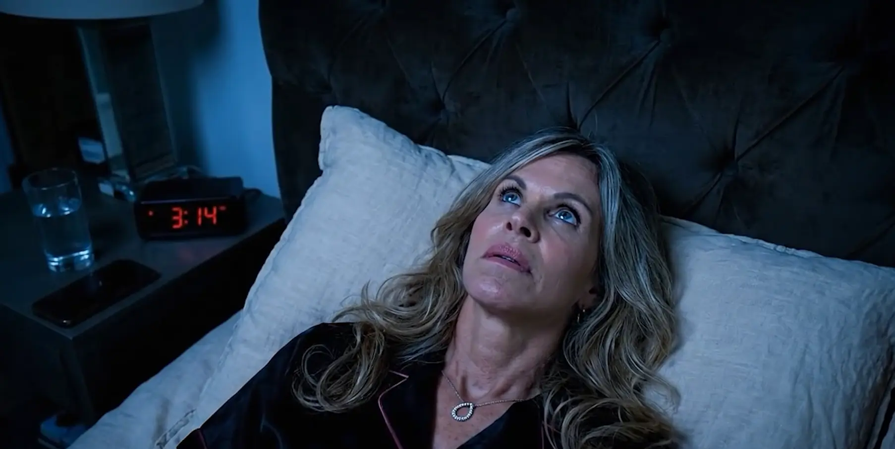 Person lying awake in bed at night unable to sleep, looking at the clock